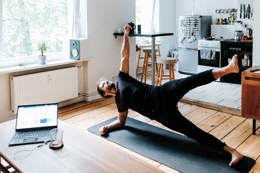 Adult man does a side plank pose during yoga workout at home office