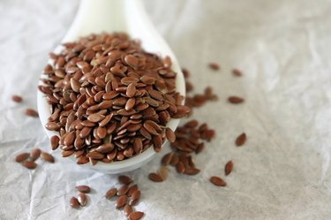 Close-up of omega-3-rich flax seeds in a ceramic spoon on white background